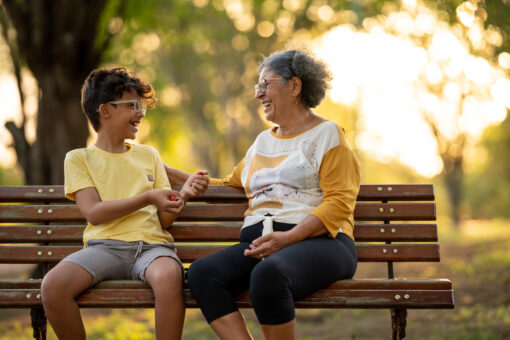 Grandmother and grandson laughing and sitting on a park bench.