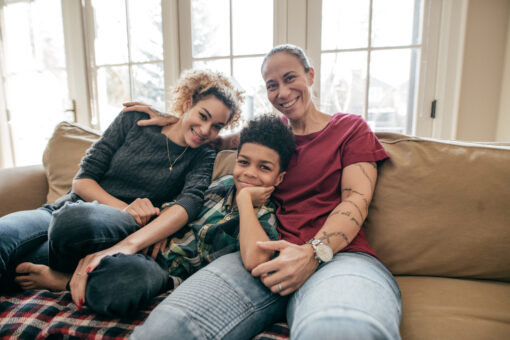 A woman sits on a sofa with a small boy and a teenage girl. They are all smiling.