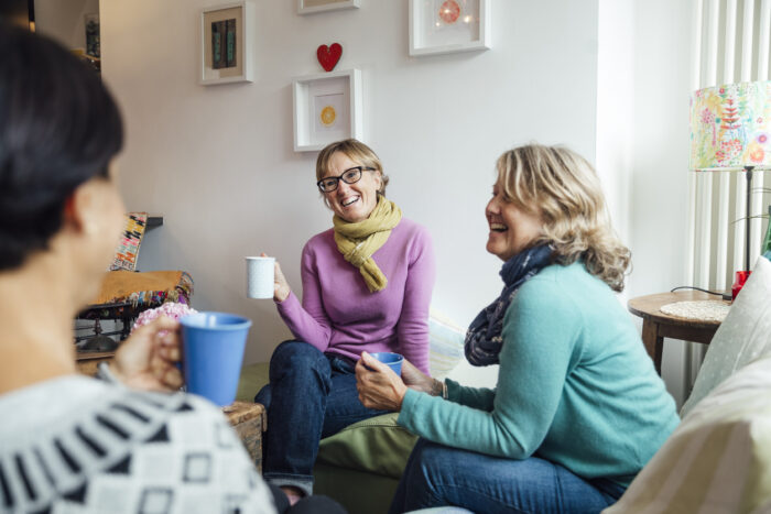 Three women sitting in a living room, drinking coffee and smiling.