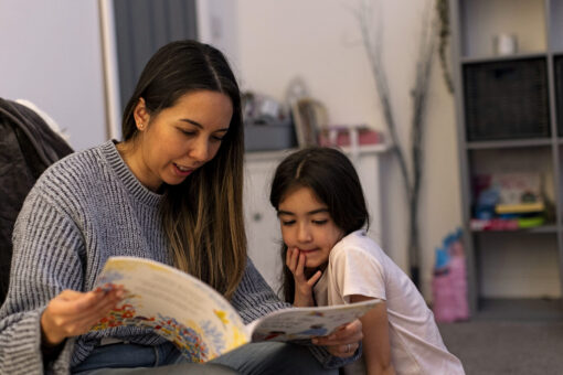 Adult sitting on a sofa reading a large book with a child